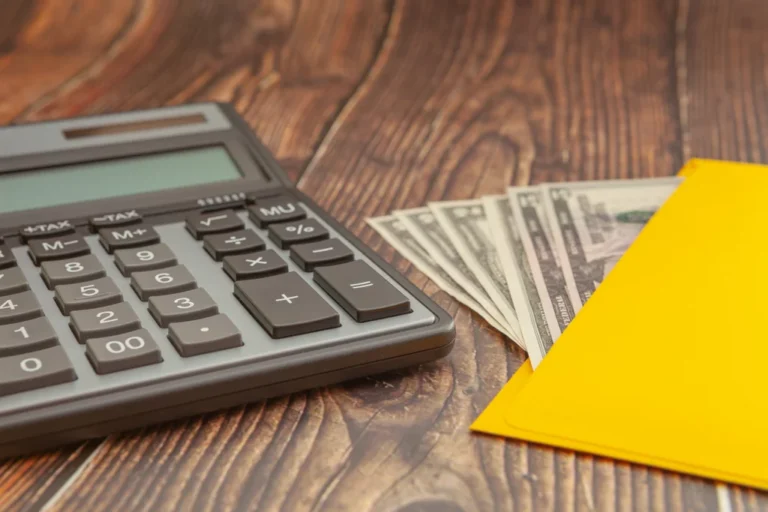Modern calculator on a wooden table with a yellow envelope and money on a blurred background, business concept, close-up
